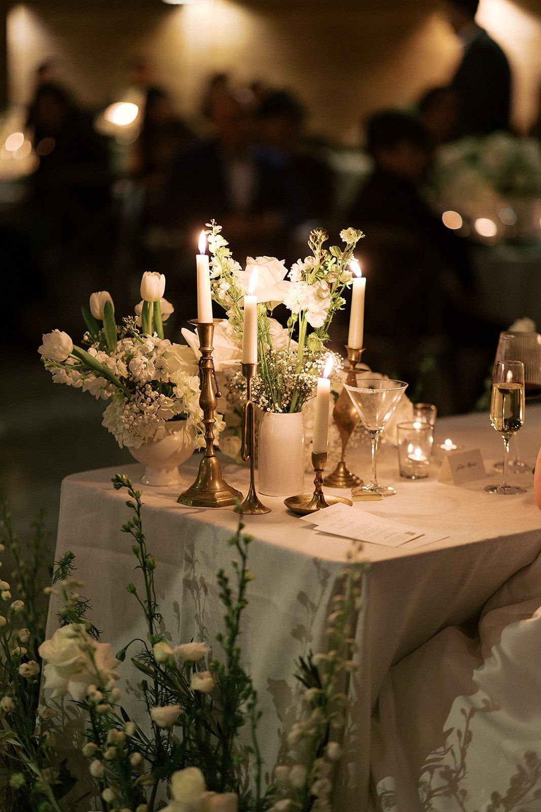 Elegant candlelit banquet table with white floral centerpiece and glassware at a dimly lit event.