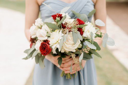 Person holding a bouquet of white and red roses with greenery, wearing a pale blue dress