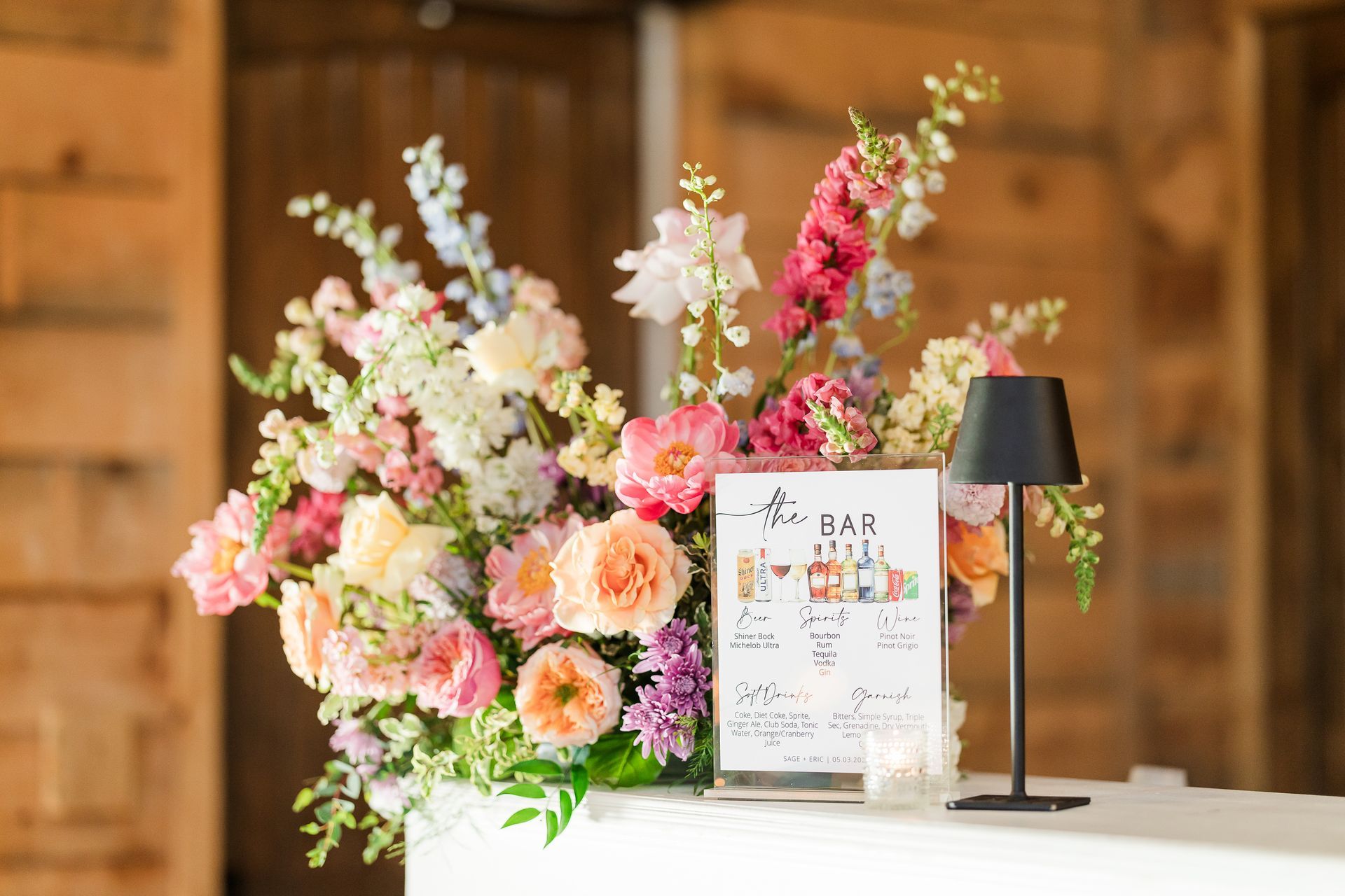 Floral display with pastel flowers and a sign on a white table against a wooden backdrop
