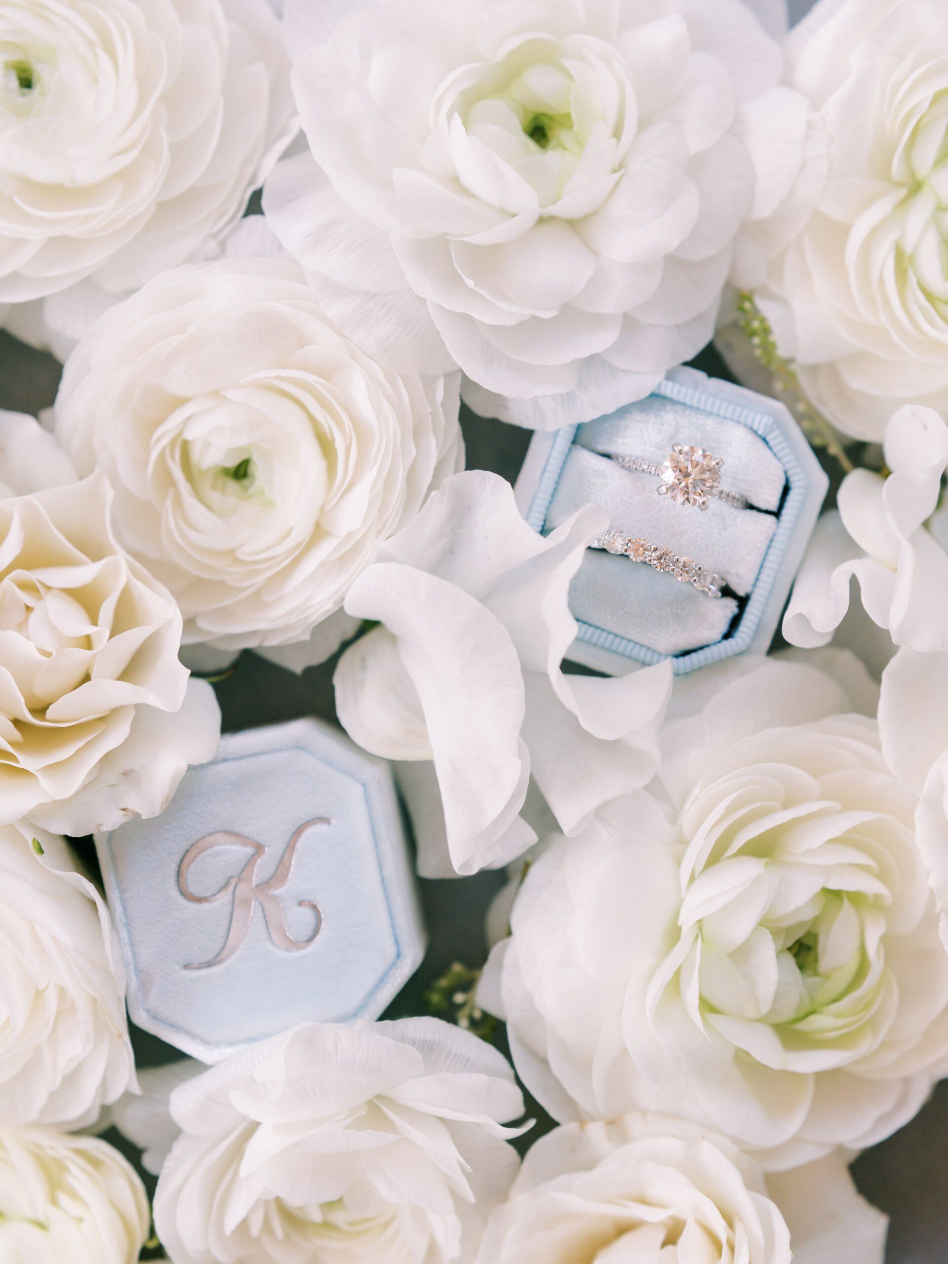 White floral arrangement with two jeweled rings on pastel blue velvet boxes