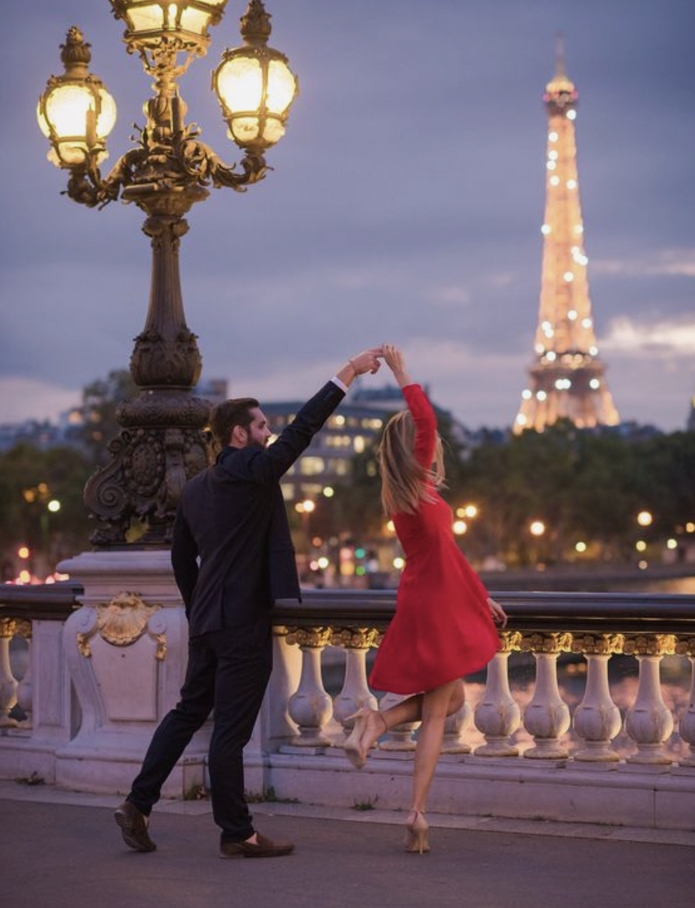 Couple dancing on a Paris bridge at dusk, with the Eiffel Tower lit in the background.