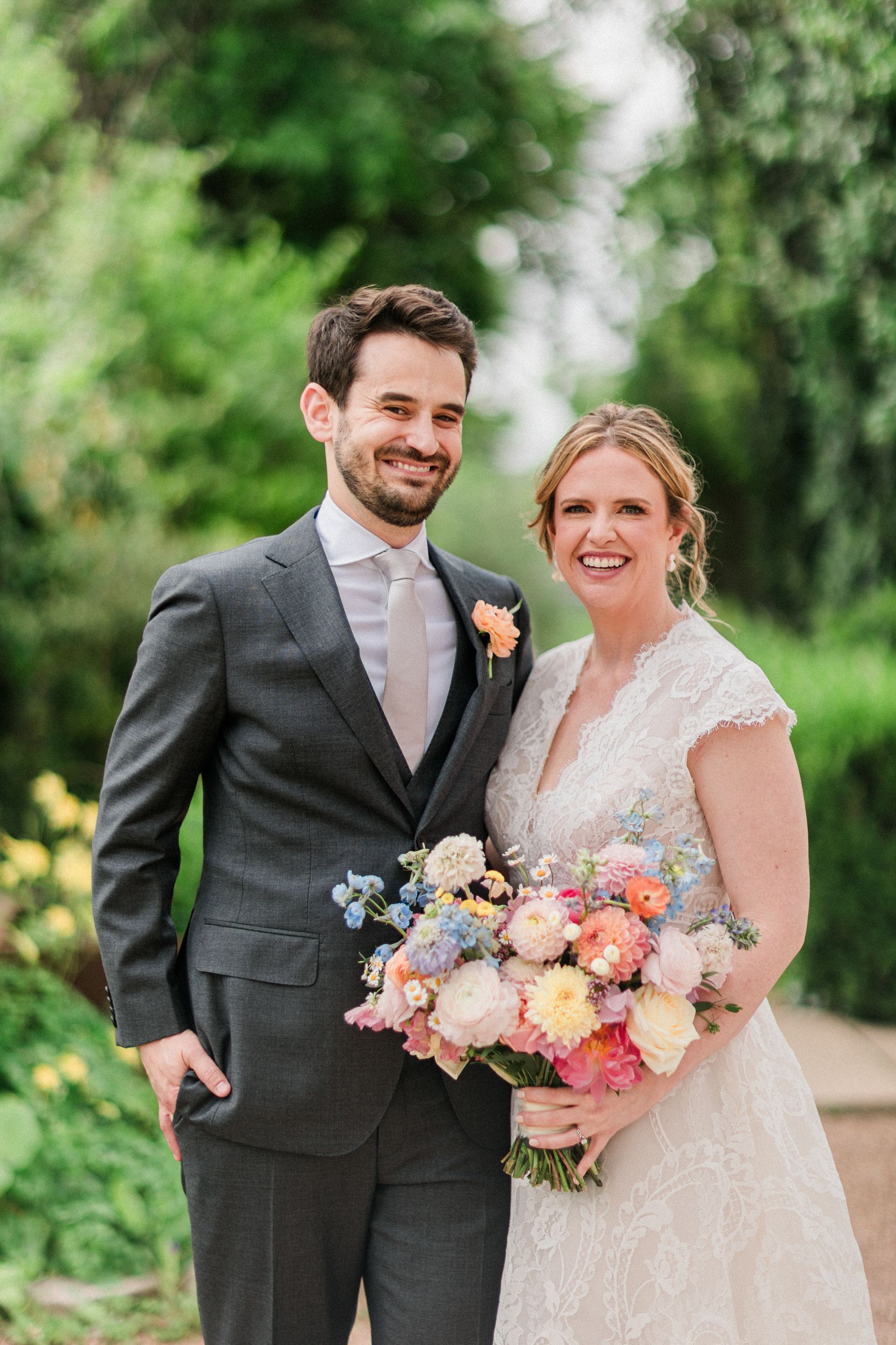 Newlyweds smiling outdoors, holding a colorful bouquet in a garden setting