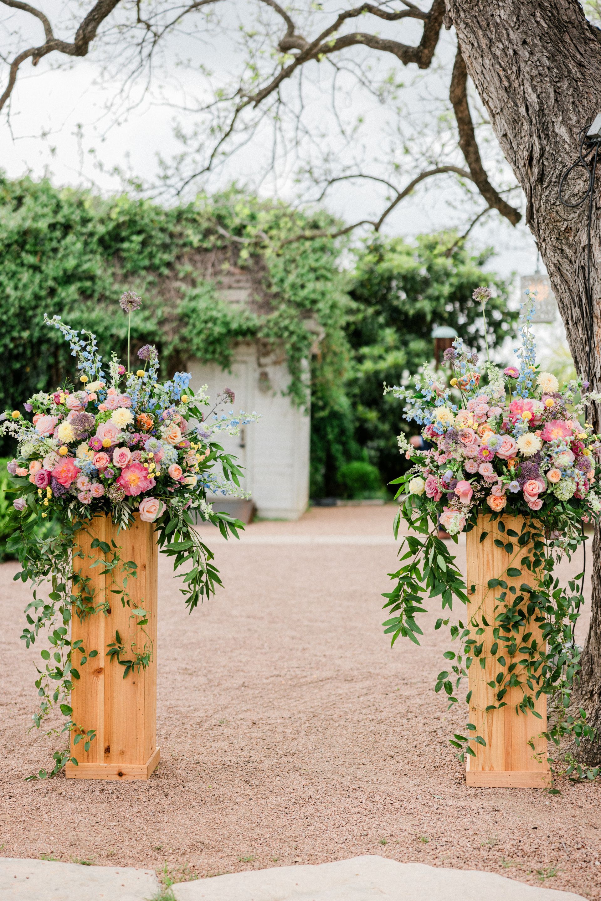 Flower-adorned wooden pedestals framing a garden path beneath trees