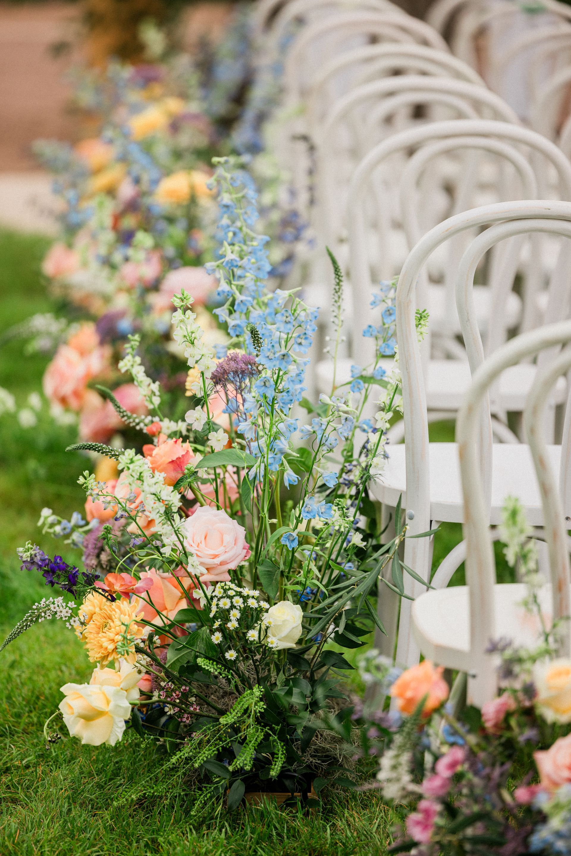 White chairs beside a garden aisle lined with pastel floral arrangements