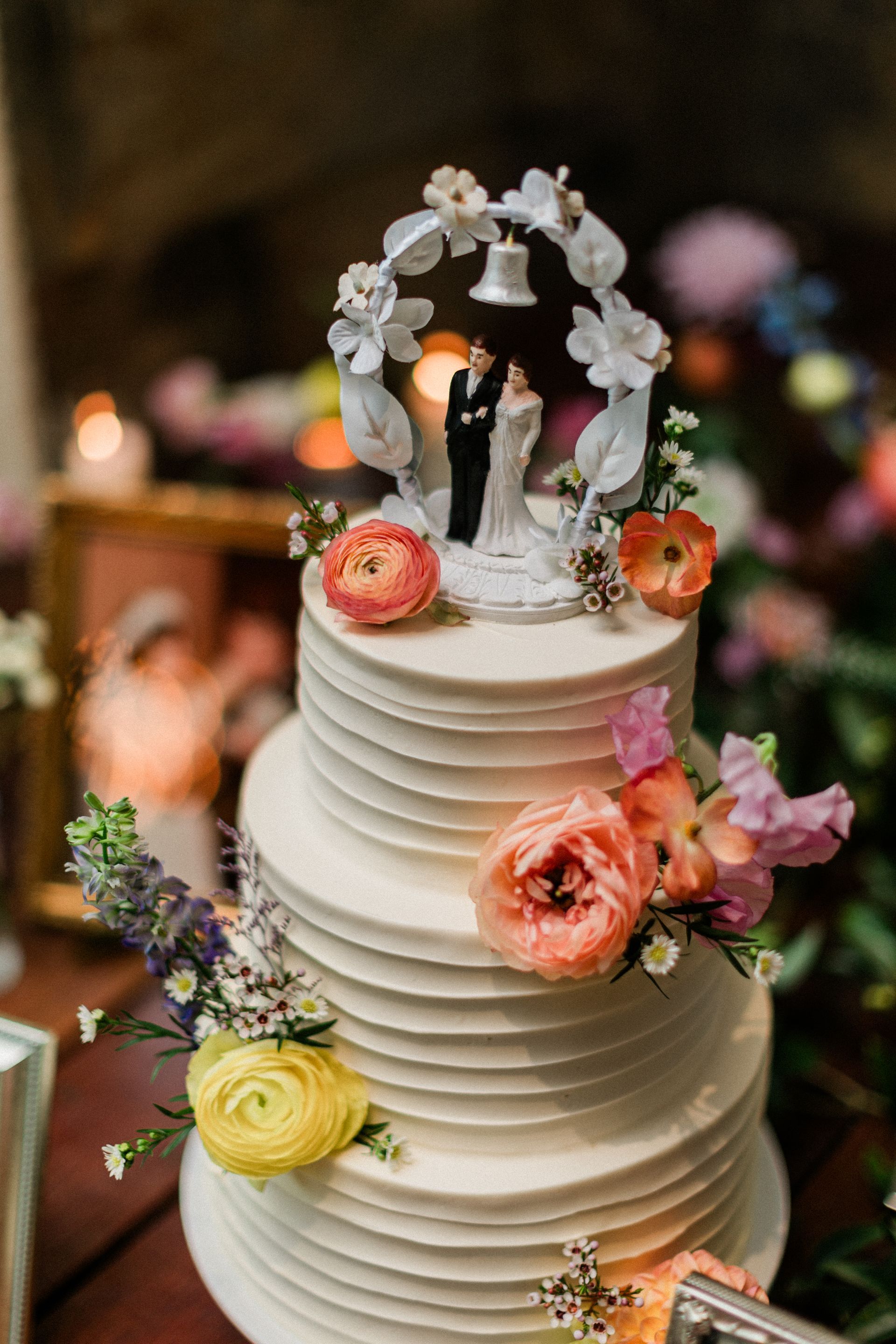 Three-tier white wedding cake with flowers and a small bride and groom topper