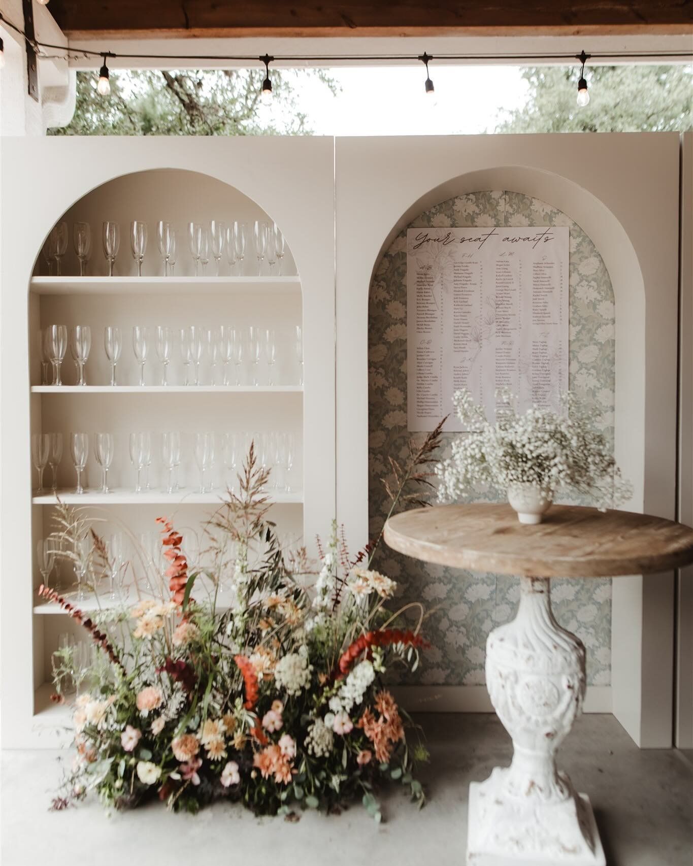 Elegant floral display beside arched shelves and a round pedestal table in a light, airy room
