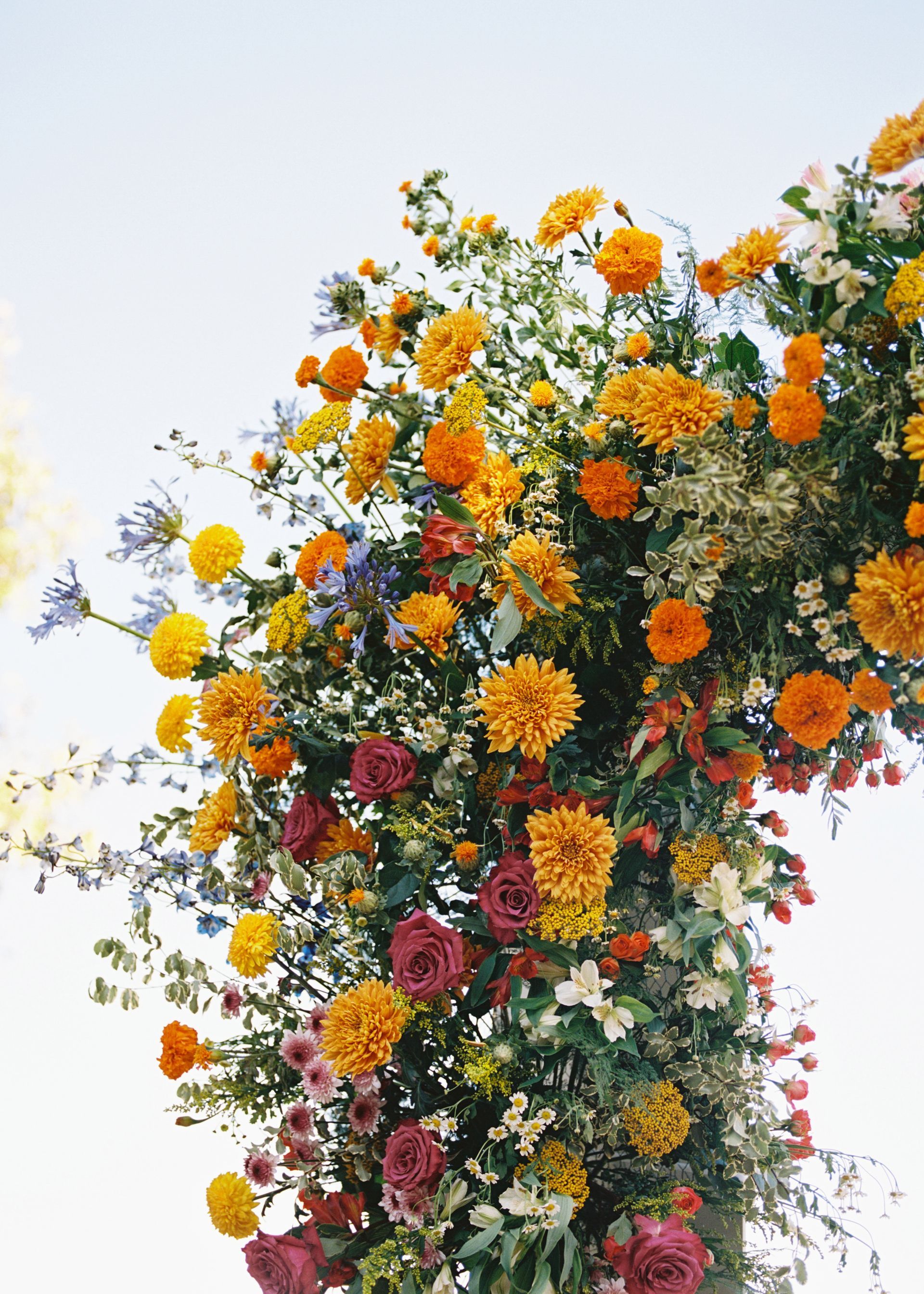 Tall floral arrangement with orange, yellow, and pink blossoms against a pale sky