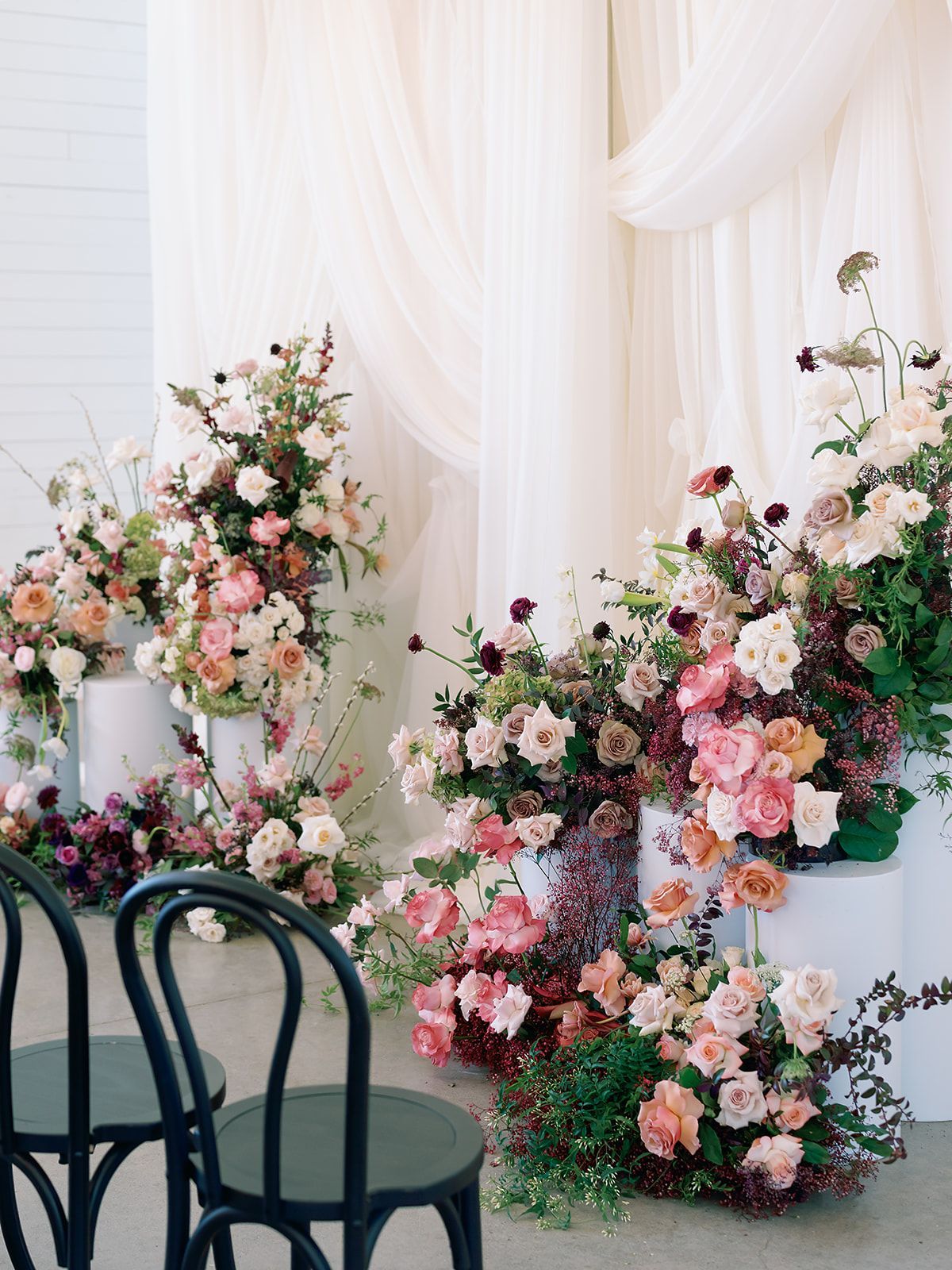 Floral event backdrop with pink and white flowers and dark green chairs in front