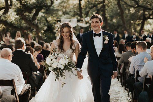Bride and groom walking down an outdoor aisle after their wedding ceremony, smiling with guests seated nearby