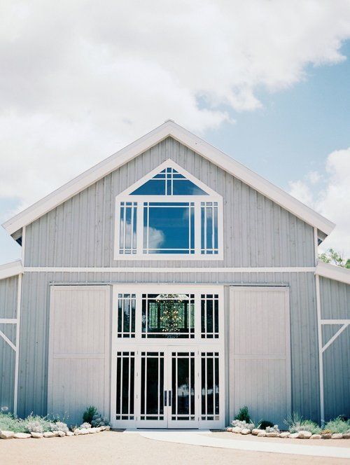 Gray barn-style building with large white-trimmed windows under a bright sky