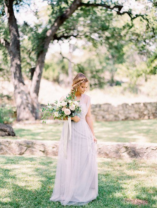 Woman in a flowing white dress holding a bouquet in a sunlit garden.