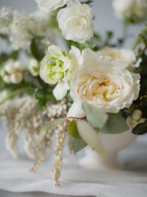 White and pale green floral bouquet with cream roses and trailing greenery on a soft fabric background