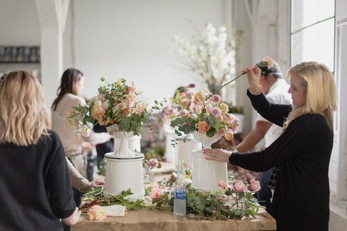 People arranging pastel floral bouquets on a table in a bright room