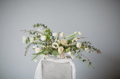 White floral arrangement with greenery on a chair against a gray background