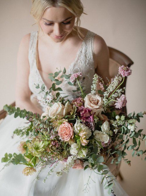 Bride holding a pastel floral bouquet, looking down in a white lace dress