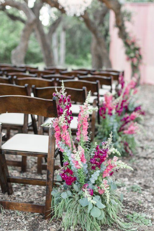 Rows of wooden chairs beside bright pink floral arrangements outdoors