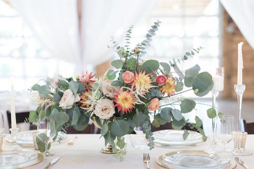 Pastel floral centerpiece on a sunlit table with glassware and candles