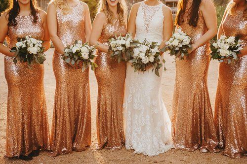 Bridesmaids in rose-gold and white dresses holding bouquets at a wedding ceremony