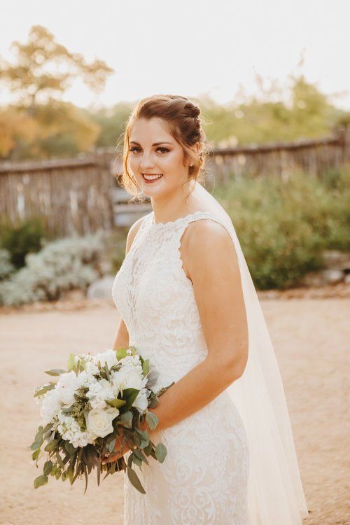 Bride in a white lace dress holding a bouquet outdoors in a garden setting