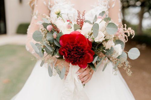 Bride holding a bouquet with red roses, white flowers, and eucalyptus