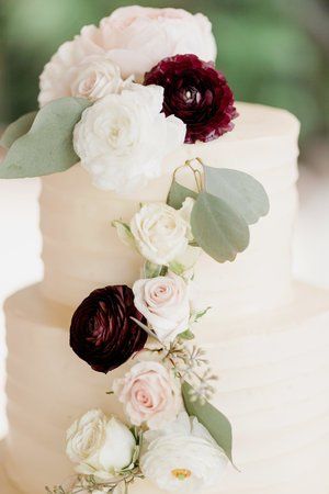 White wedding cake with cascading cream and burgundy flowers and green leaves