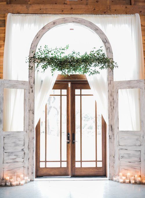 White draped wedding arch with greenery and wooden double doors in a bright indoor venue