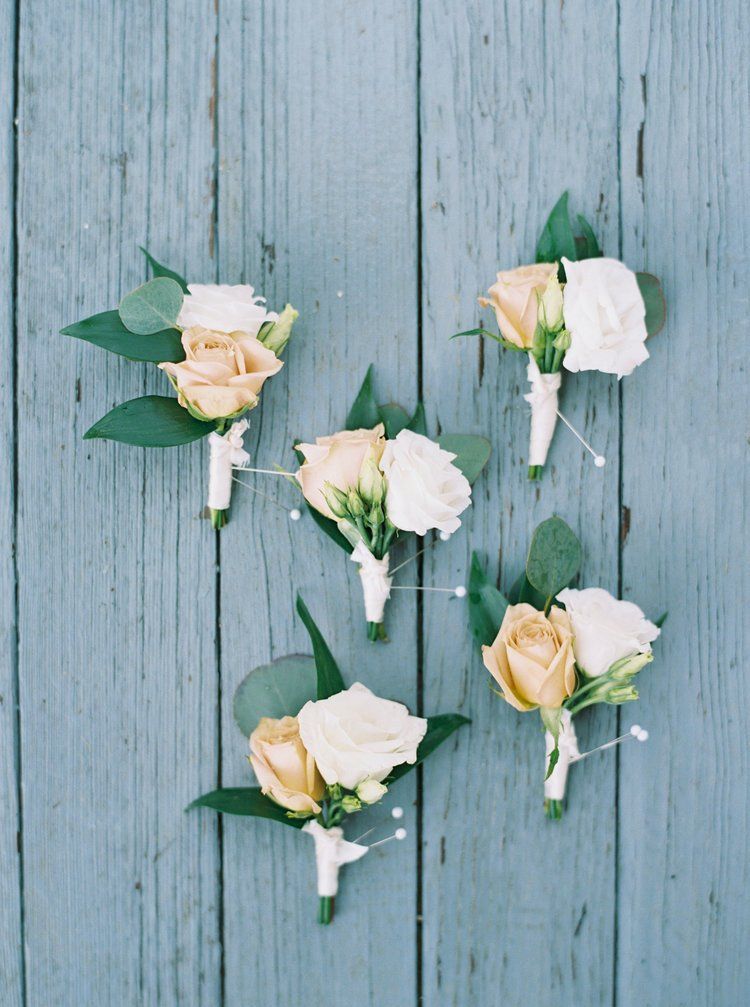 Five cream and pale yellow rose boutonnieres on a blue wooden surface