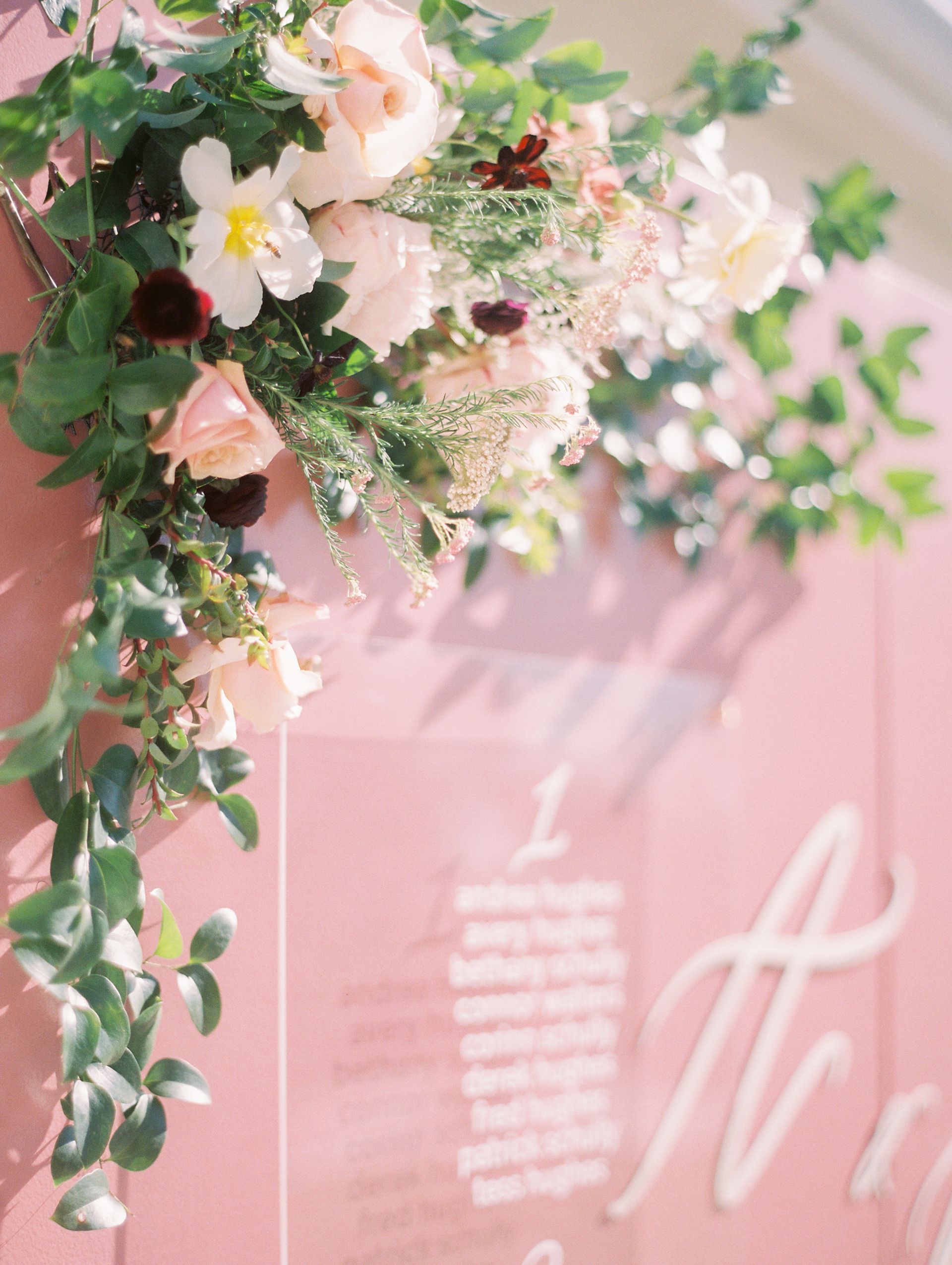 Pastel floral arrangement with pink roses and greenery beside a soft pink wedding sign