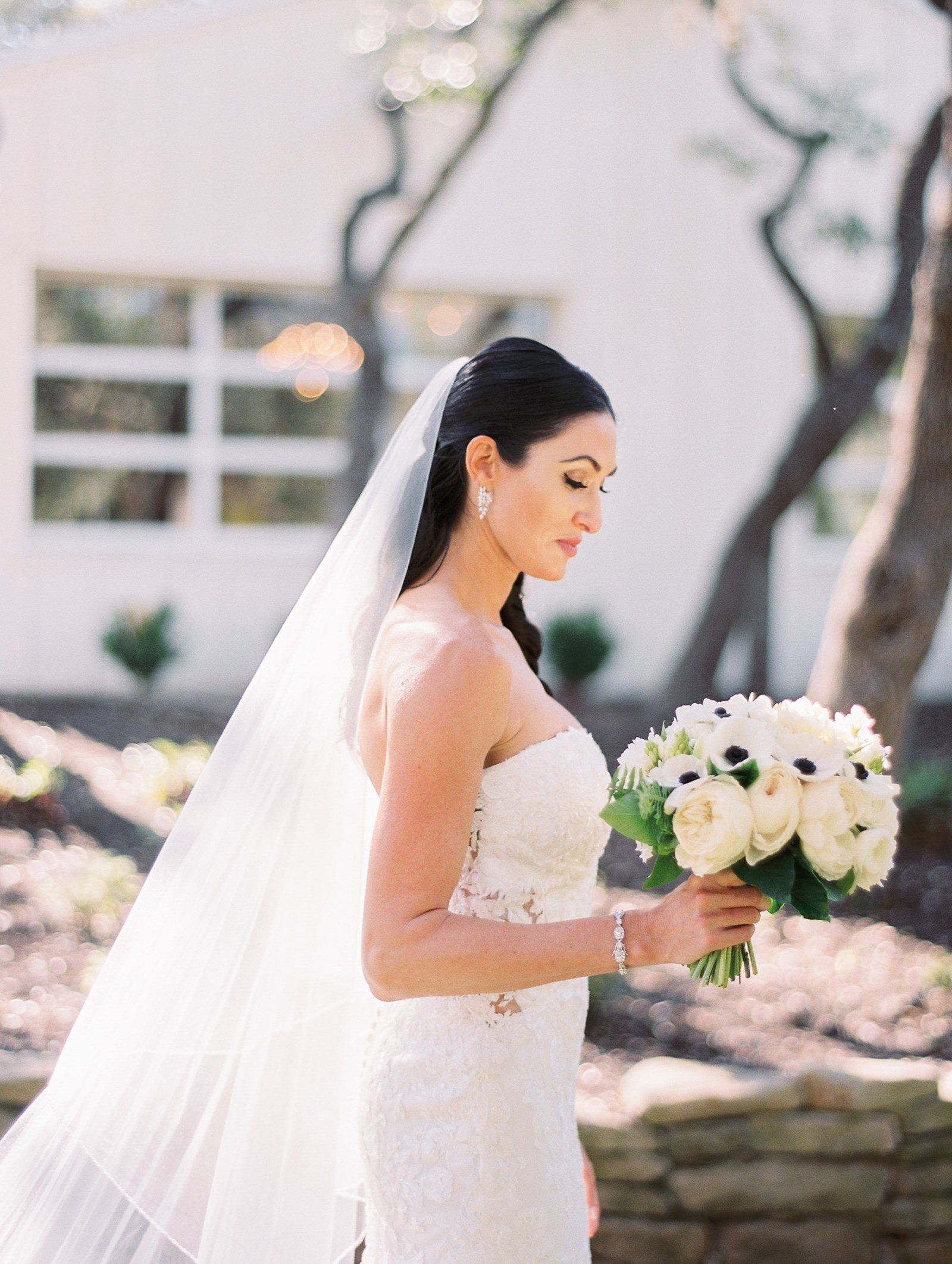 Bride in a white dress holding a bouquet outdoors, wearing a long veil.
