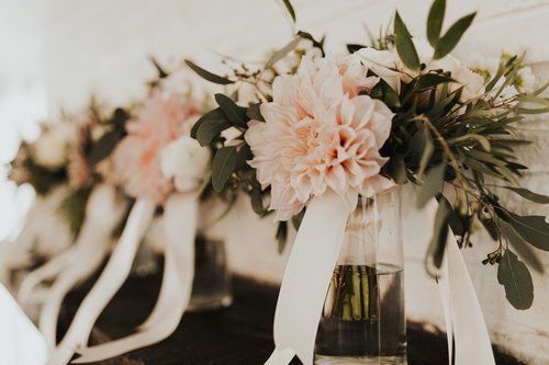 Soft pink floral bouquets in glass vases with white ribbons on a table