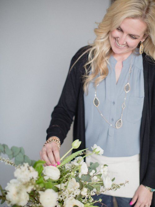 Woman arranging a white floral bouquet in a light-filled room, smiling and looking down