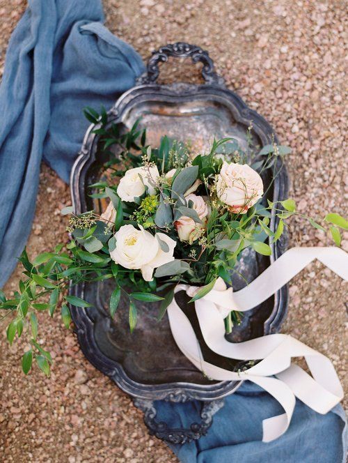 White rose bouquet in a decorative silver tray with blue ribbon on a textured ground