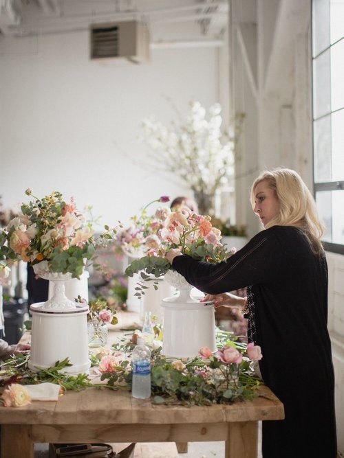 Person arranging pastel flower bouquets on a wooden table in a bright studio