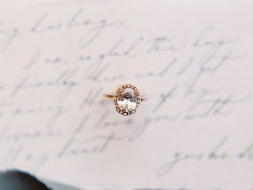Gold ring with a clear gemstone resting on a handwritten page of paper.