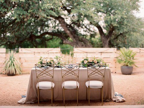 Outdoor dining table set with beige chairs in a backyard patio, surrounded by potted plants and a wooden fence