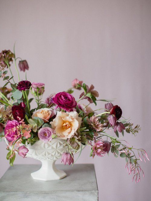 Elegant pink, white, and peach floral arrangement in a white pedestal vase on a gray table