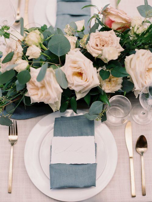 Elegant table setting with white roses, blue napkin, white plates, and gold utensils
