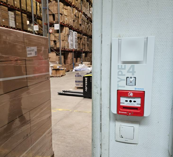 A type 4 fire alarm is mounted on a wall in a warehouse