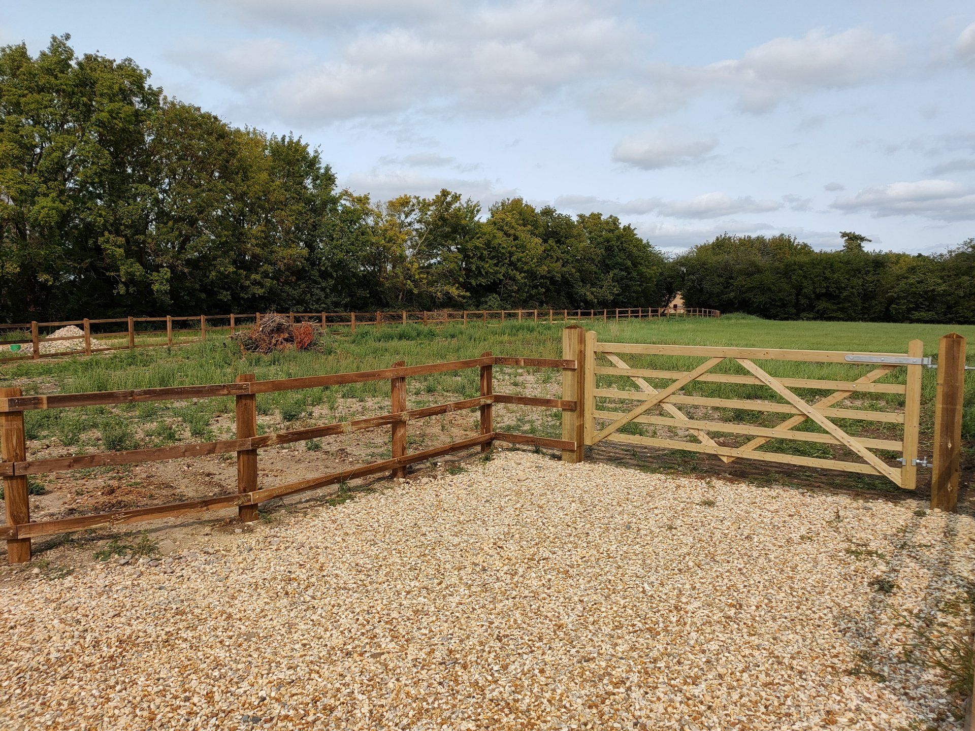 Three bar, 4 foot high fence around the edge of a field, with a gate.