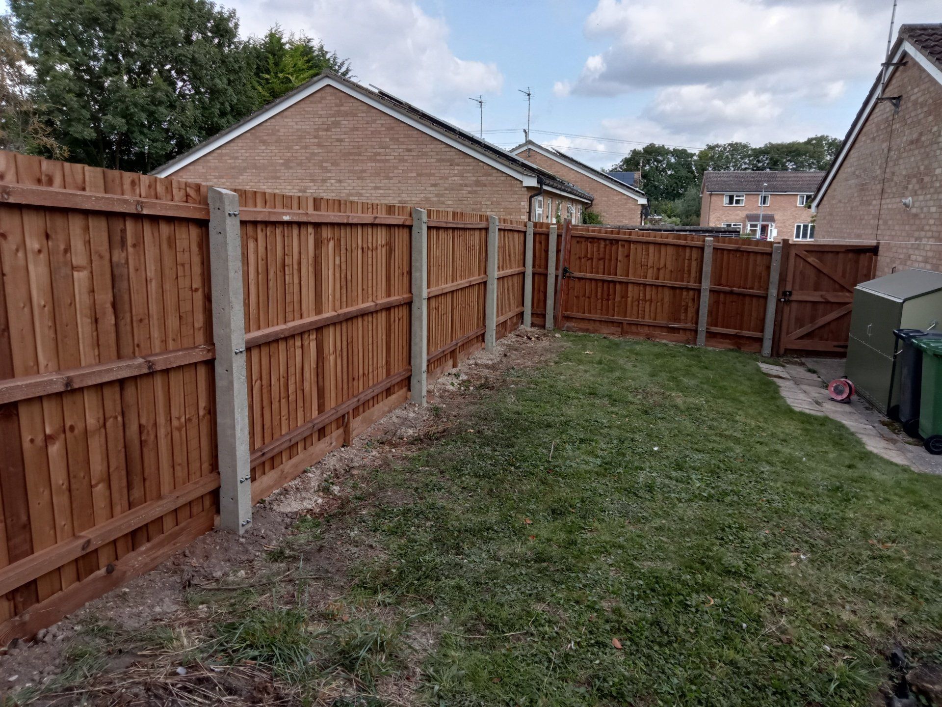 A concrete post fence with wooden gravel board and feather edge fencing applied to rails as seen from inside.