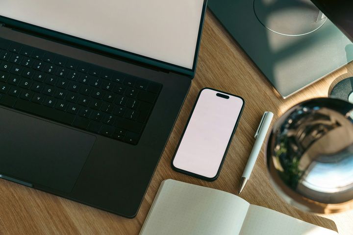 Desk with laptop, smartphone, notebook, pen, and coffee cup on a wooden tabletop.