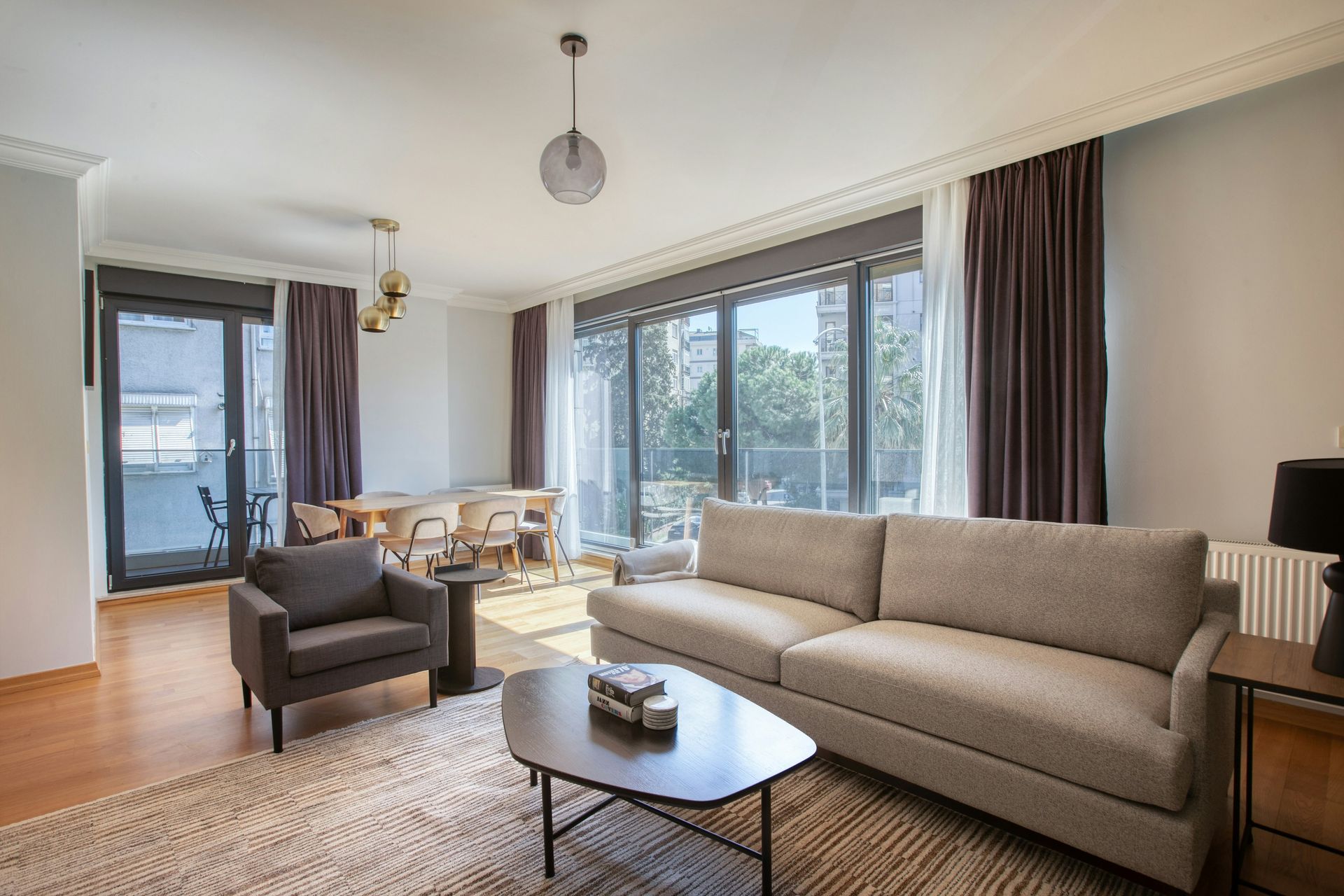 Bright living room with gray sofa, armchair, coffee table, large windows, and balcony doors
