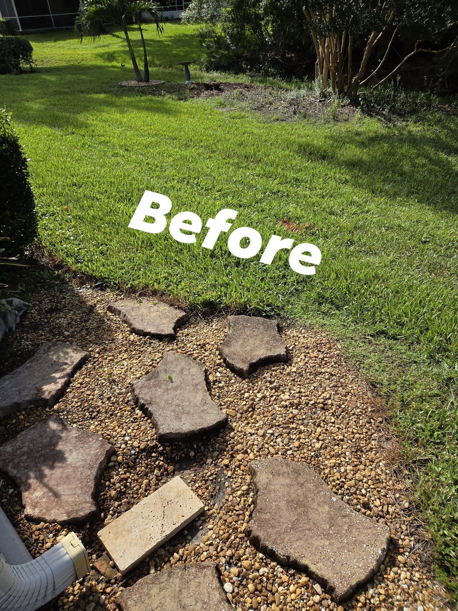 Lawn with stone pavers and gravel path, bordered by green grass and trees.