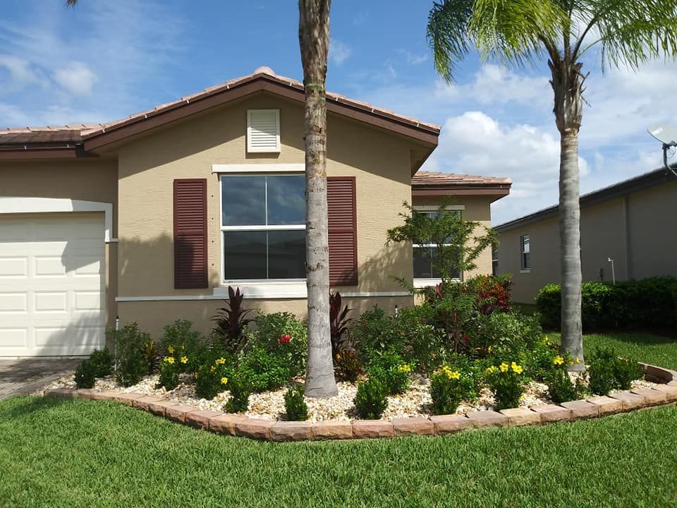 Tan house with brown shutters and a landscaped front yard with flowers.