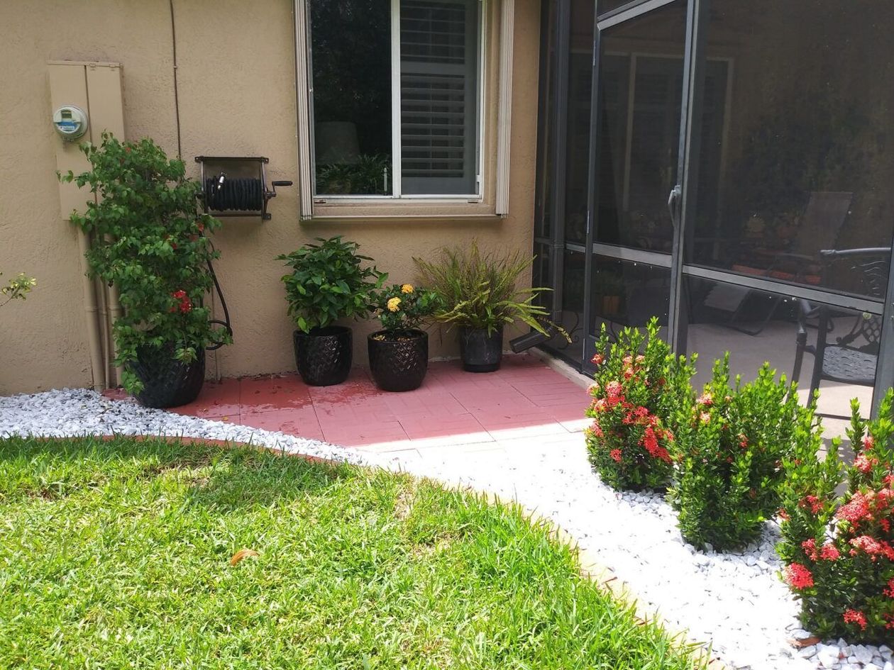 Backyard patio with potted plants, red pavers, white rocks, green grass, and screen enclosure.