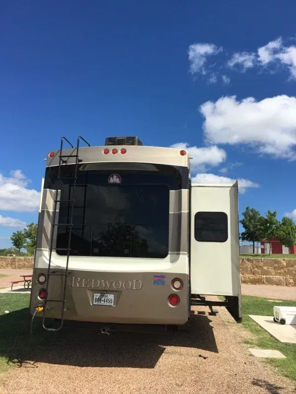 Rear view of a beige RV with a side door open, parked on a sunny driveway under a blue sky.