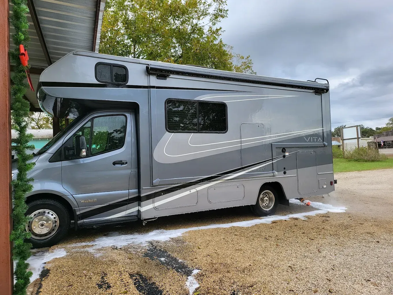 Silver RV parked on a gravel lot with water pooled underneath and beside it