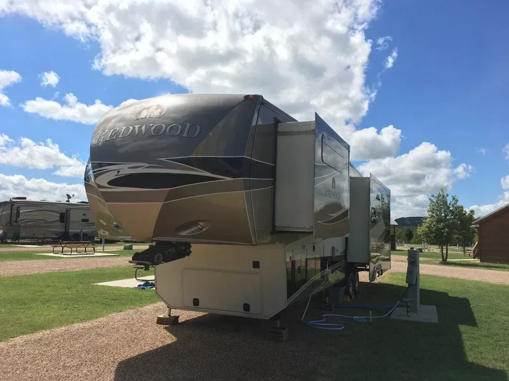Large beige and black RV trailer parked on grass under a blue sky with clouds