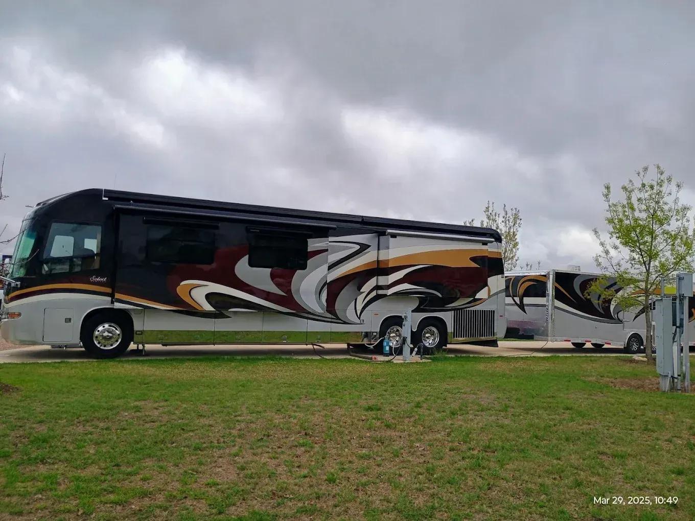Large black and white motorcoach parked on a grassy lot under a cloudy sky