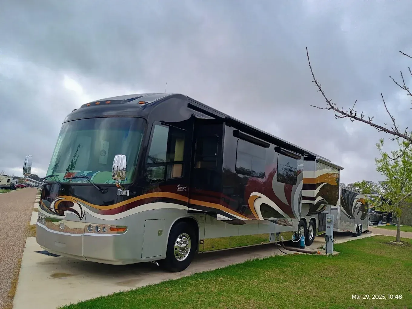 Large white and black motorhome parked outdoors by a curb, with a person standing beside it.